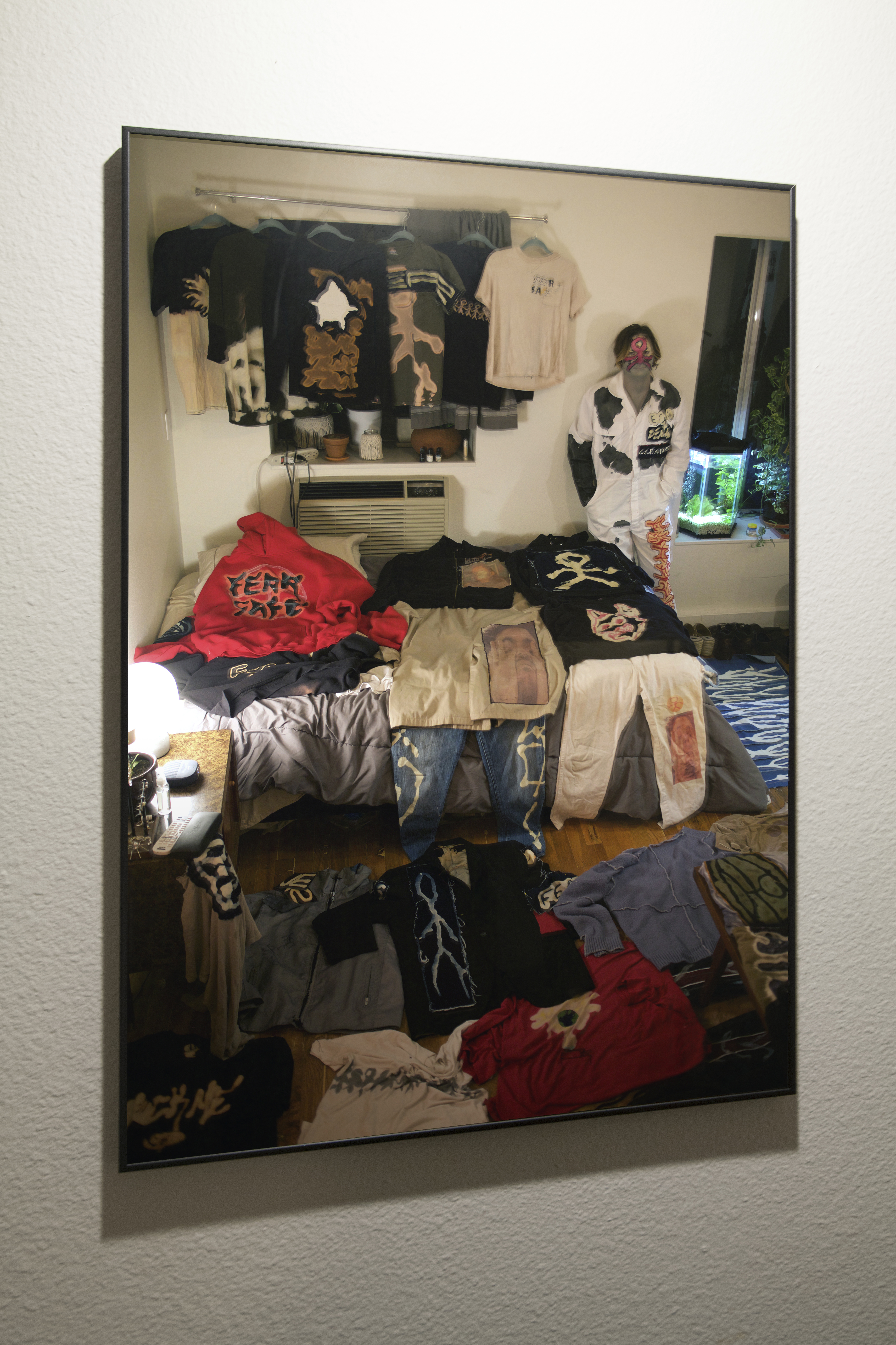 Framed photo print of a bedroom with Fear Safe clothing scattered everywhere hung on a white wall